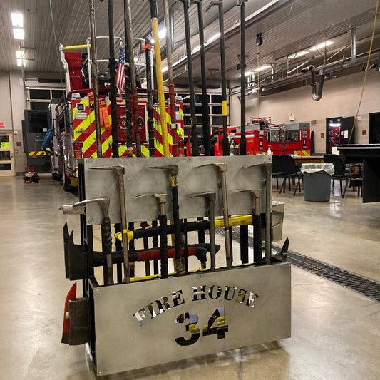 A metal fire tool rack with various firefighter tools attached to it, positioned in a fire station garage.